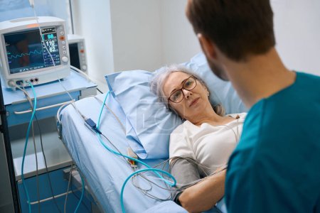 Une dame âgée est connectée à un moniteur de patient, une jeune infirmière est à proximité