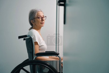 Photo for Elderly lady with glasses sits in a wheelchair, the woman is in the rehabilitation department - Royalty Free Image