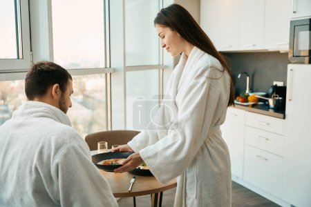 Téléchargez les photos : Femme attentionnée traite son mari à un petit déjeuner traditionnel dans un environnement agréable, le couple est situé dans une cuisine confortable - en image libre de droit