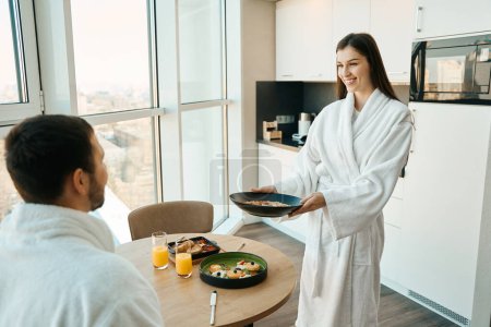 Téléchargez les photos : Femme traite son mari bien-aimé avec un petit déjeuner traditionnel dans une atmosphère confortable, couple est situé à grande fenêtre de vue - en image libre de droit