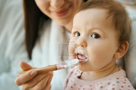 Photo for Smiling woman feeding a small child with a small spoon, the baby has chubby cheeks - Royalty Free Image