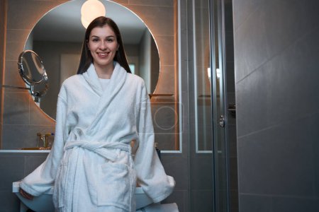 Téléchargez les photos : Jeune brune en bonne santé se tient dans la salle de bain, une femme en peignoir - en image libre de droit