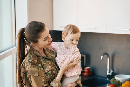 Téléchargez les photos : Soldat souriant tenant une jolie fille dans ses bras, maman en uniforme militaire - en image libre de droit