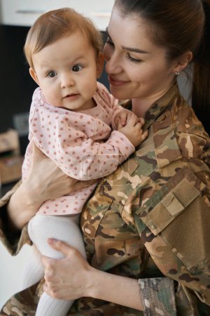 Foto de Mujer militar joven sostiene a una niña en sus brazos, una madre con un uniforme de camuflaje - Imagen libre de derechos