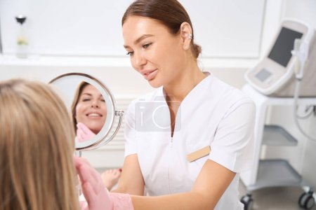 Téléchargez les photos : Une femme cosmétologue consulte une patiente en peignoir, une employée en uniforme médical - en image libre de droit