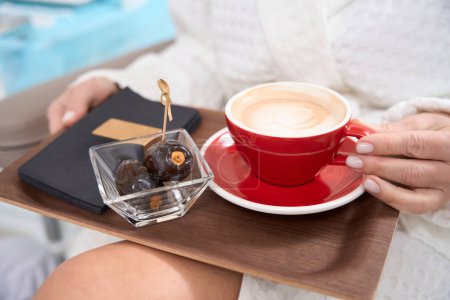 Téléchargez les photos : Femme en peignoir s'assoit avec une tasse de café et de fruits, sur un plateau de serviettes - en image libre de droit
