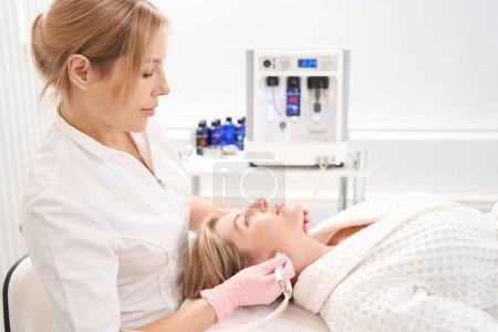 Kosmetikerin arbeitet mit der Gesichtshaut der Patientin, der Spezialist verwendet CO2-Laser
