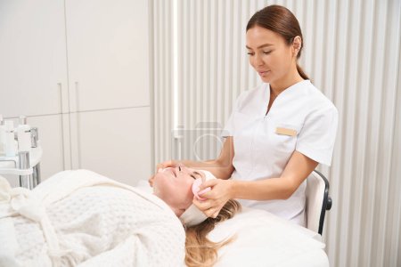 Foto de Mujer en una sesión de procedimientos de atención en una clínica de medicina estética, un cosmetólogo quita una máscara con discos especiales - Imagen libre de derechos