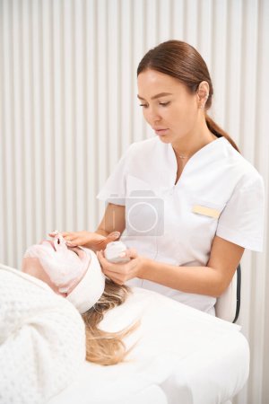 Foto de Cosmetólogo aplica un suero especial a la piel de la cara de los pacientes, se realiza un procedimiento eficaz de perfusión dérmica - Imagen libre de derechos