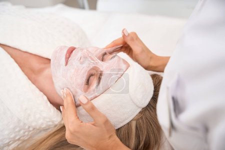 Téléchargez les photos : Femme se couche sur un canapé de cosmétologie avec du sérum sur le visage, une patiente en perfusion cutanée - en image libre de droit