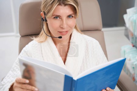 Photo for Beautiful woman sitting in chair with forbrein headset, female patient in bathrobe - Royalty Free Image