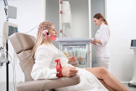 Foto de Diagnóstico femenino en un centro de rehabilitación realiza un procedimiento de electroencefalograma en una paciente, una mujer con una gorra con electrodos - Imagen libre de derechos