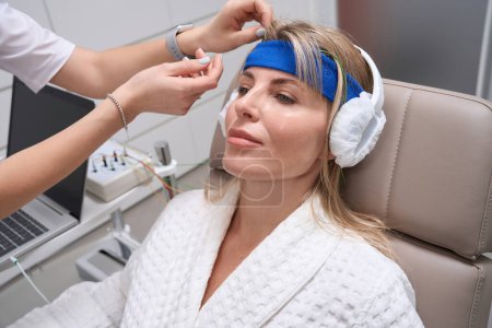 Foto de Mujer hermosa en el procedimiento de corrección bioacústica en un centro médico, se utiliza un auricular especial - Imagen libre de derechos