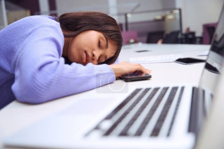 Téléchargez les photos : Fatiguée travailleuse dans des vêtements élégants posé sa tête sur les mains et dormir au bureau de l'espace ouvert - en image libre de droit