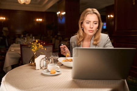 Photo for Concentrated business woman working on important project on laptop during dinner at lobby bar - Royalty Free Image