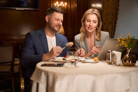 Téléchargez les photos : Couple marié choisissant sur ordinateur portable endroit pour se reposer pendant les vacances pendant le déjeuner dans le café, réservation de billets et hôtel - en image libre de droit