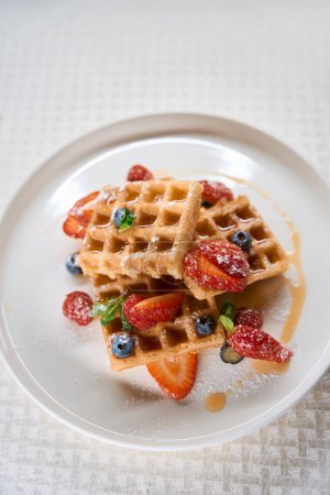 Téléchargez les photos : Gaufres belges sucrées avec fraises, bleuets et sirop dans l'assiette, menu du petit déjeuner au café - en image libre de droit