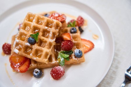 Photo for Close-up delicious crunchy waffles with strawberries, blueberries and honey on plate, seasonal menu - Royalty Free Image