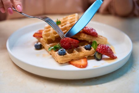 Photo for Close-up female hands cutting off piece of waffle with berries ty try, seasonal dish in restaurant - Royalty Free Image
