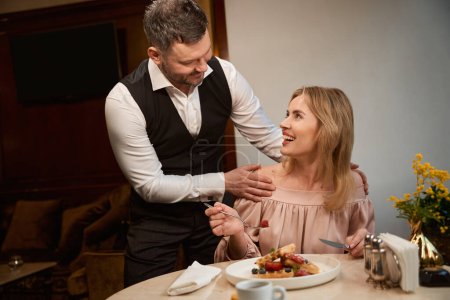 Téléchargez les photos : Homme étreignant sa belle petite amie par les épaules au restaurant, faisant la surprise sur le déjeuner - en image libre de droit