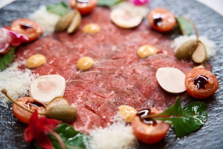 Photo for Close-up cold appetizer beef carpaccio with parmezan, capers and cherry tomatoes on black plate - Royalty Free Image