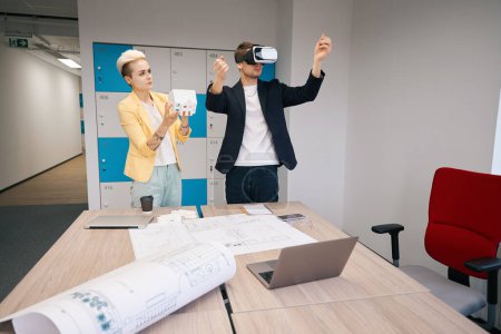 Foto de Cliente masculino revisando su futura casa de pie en gafas de realidad virtual en oficina de diseño, cooperación, efectos visuales - Imagen libre de derechos