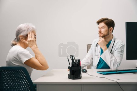 Photo for Elderly patient complains to the doctor about a headache, the therapist conducts an appointment in a medical center - Royalty Free Image