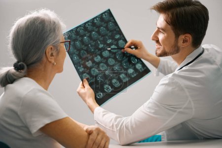 Photo for Therapist holds an MRI scan of the brain in his hands, he consults an elderly patient - Royalty Free Image