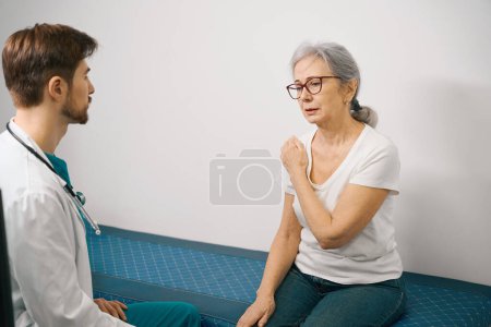Photo for Pensioner at a traumatologists appointment in a medical center, a woman complains of pain in her shoulder joint - Royalty Free Image