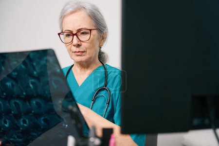 Foto de Hermosa doctora anciana sostiene una resonancia magnética del cerebro en sus manos, una mujer con gafas elegantes - Imagen libre de derechos