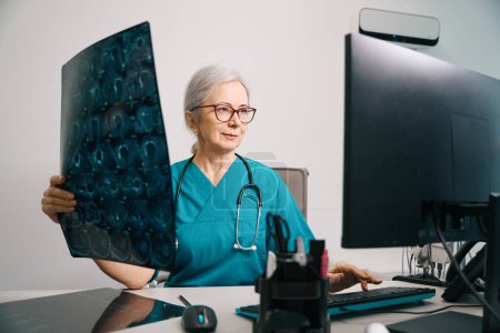 Terapeuta experimentada sostiene una resonancia magnética en sus manos, una mujer usa una computadora