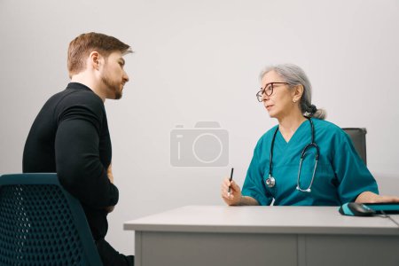 Téléchargez les photos : Jeune homme barbu à un rendez-vous chez le thérapeute, un homme se plaint de douleurs épigastriques - en image libre de droit