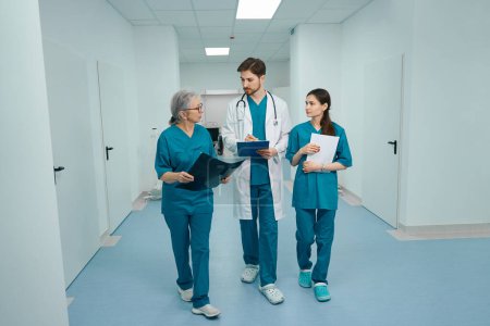 Photo for Medical colleagues are walking along the corridor of diagnostic department, the doctors have folders in their hands, MRI scans, documents - Royalty Free Image
