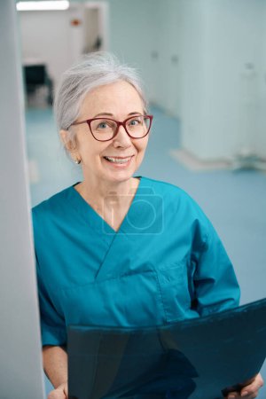 Téléchargez les photos : Femme souriante se tient dans le couloir de l'hôpital avec IRM scan, dame avec des lunettes - en image libre de droit