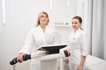 Téléchargez les photos : Femme agréable dans un centre médical subit une procédure de diagnostic bioimpedancemetry, un spécialiste utilise un bioimpedancemeter - en image libre de droit