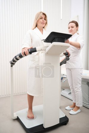 Téléchargez les photos : Femme diagnosticien effectue une procédure de diagnostic bioimpedancemetry, le médecin utilise un équipement moderne - en image libre de droit