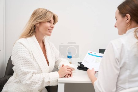 Foto de Dos hermosas mujeres están sentadas en un escritorio en un centro médico, un médico diagnostico consulta a una paciente femenina - Imagen libre de derechos