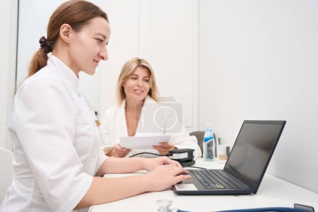 Foto de Dos mujeres jóvenes están sentadas en un escritorio en un centro médico, un especialista consulta a una paciente - Imagen libre de derechos
