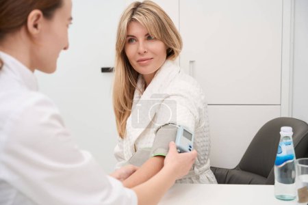Foto de Mujer médico mide la presión arterial de un paciente con un tonómetro, las mujeres están en el departamento de diagnóstico - Imagen libre de derechos