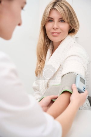 Foto de Médico femenino mide la presión arterial a un paciente con un tonómetro, las mujeres están en el departamento de diagnóstico - Imagen libre de derechos
