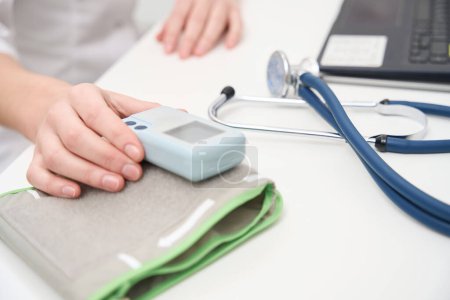 Téléchargez les photos : Médecin sur le lieu de travail avec tonomètre et stéthoscope, à côté d'un ordinateur portable moderne - en image libre de droit