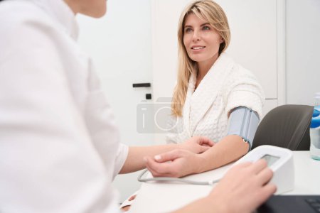 Foto de Trabajador de la salud mide la presión arterial a un paciente con un tonómetro, una mujer en un albornoz - Imagen libre de derechos