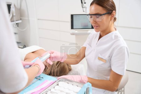 Photo for Assistant passes the instrument for the cosmetic procedure to the esthetician, the staff uses CO2 laser - Royalty Free Image