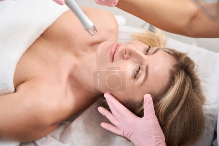 Foto de Señora en el procedimiento de rejuvenecimiento de la piel láser, cosmetólogo femenino en guantes de protección utiliza láser de CO2 - Imagen libre de derechos