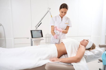 Foto de Mujer en la clínica sobre el procedimiento de descamación láser después del parto estrías, el personal utiliza equipos modernos - Imagen libre de derechos