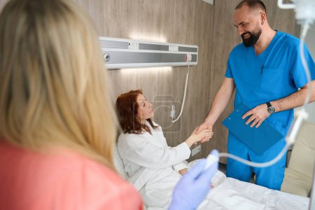 Téléchargez les photos : Bon médecin et femme mûre client serrant la main dans la chambre moderne de l'hôpital - en image libre de droit