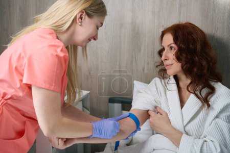 Foto de Enfermera bonita en uniforme de trabajo y guantes que proporcionan atención médica a hermosa visitante mujer en el centro médico - Imagen libre de derechos