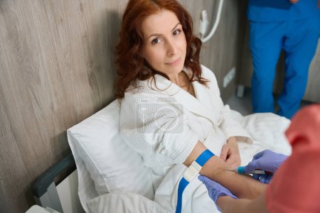 Foto de Señora madura en bata frente a la cámara mientras el médico le hace la inyección en el centro de salud - Imagen libre de derechos