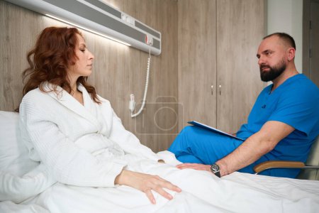Photo for Attractive woman lost in thought while receiving treatment by attentive doctor in modern room of hospital - Royalty Free Image