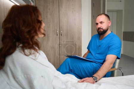 Photo for Young medical specialist providing medical care to female patient in modern room of hospital - Royalty Free Image